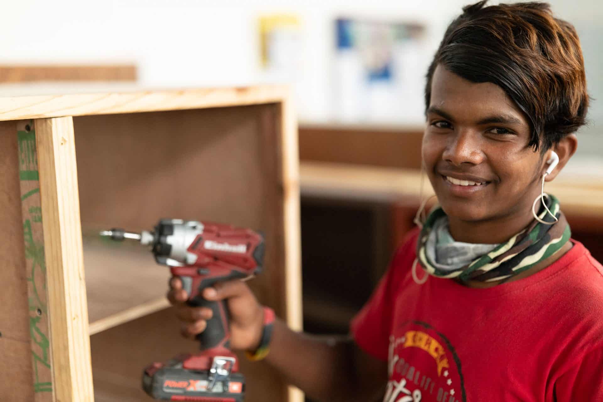 Boy from Himalayan Life Vocation Training Program in Nepal holds up a screwdriver as he learns how to put together a bookcase