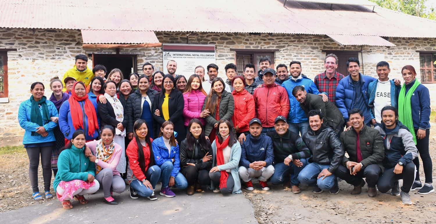 Himalayan Life staff members gather for a group photo in front of a brick school building