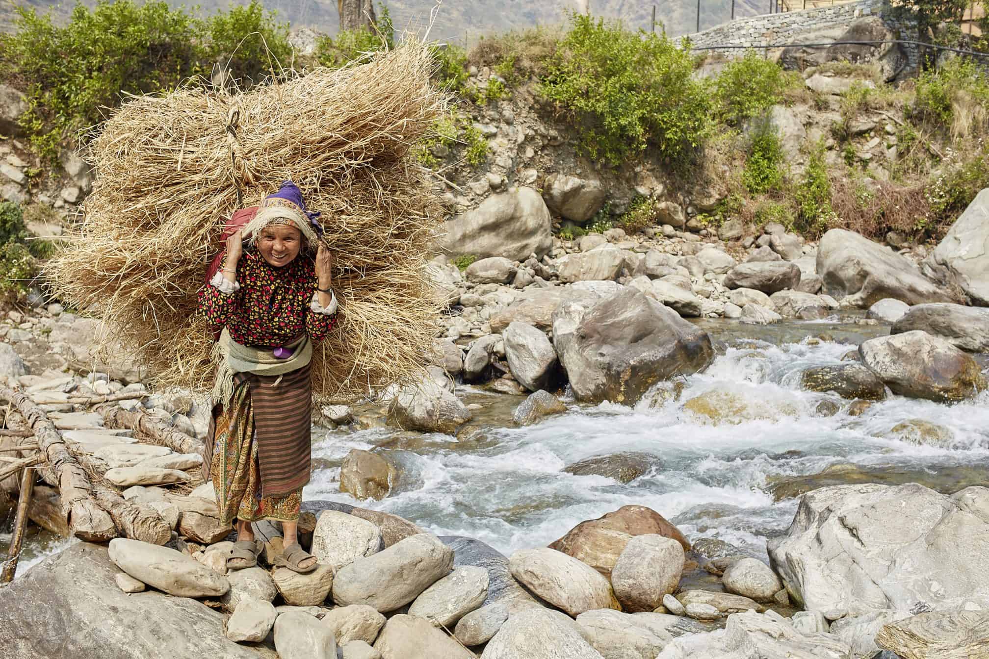 woman carrying logs across a mountain stream